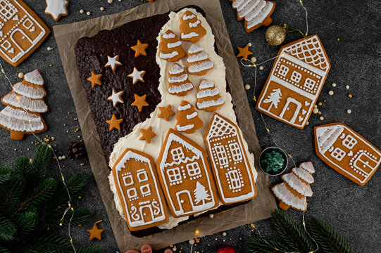 Christmas chocolate cake with cream, decorated with gingerbread cookies on top on dark background. Top view, copy space.