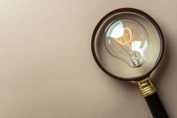 Glowing light bulb is magnified by magnifying glass on beige background, symbolizing bright ideas and creative thinking in simple and clear composition