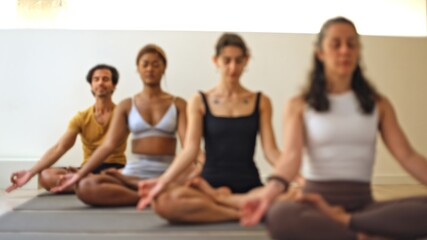 Blurred image of a diverse group meditating peacefully in a bright room.
