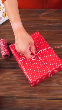 Female hands wrapping Christmas gift in craft ecological paper on dark wooden background with decorating elements, Christmas or New year DIY packing.