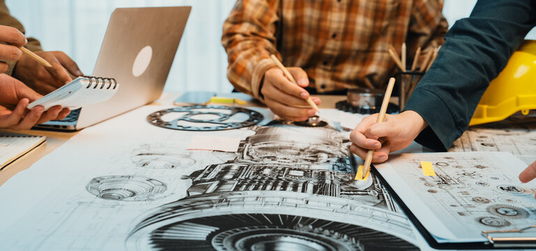 A group of engineers collaborates on detailed technical drawings and blueprints in a bright office, showcasing teamwork and creativity in machinery design and development. SACTR