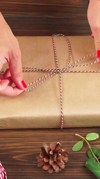 Vertical video of Woman s hands wrapping Christmas gift on dark wooden background.