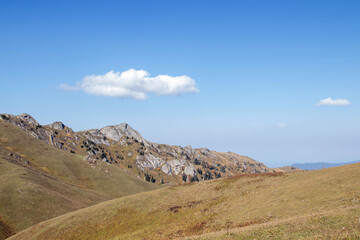 Mountain landscape with rocky outcrops, rugged hills, sparse vegetation and coniferous trees under clear blue sky