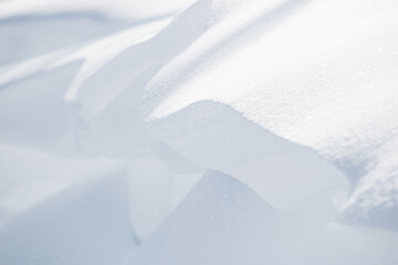 Wind blowing fine white snow off edge of large winter snowdrift