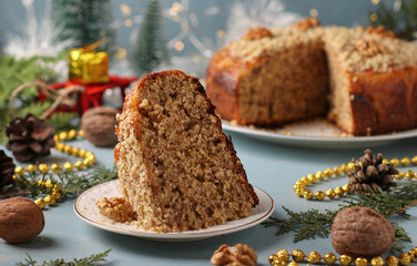Festive pie with apples, walnuts and cinnamon, sprinkled nuts with cut piece on light blue background. New year still life