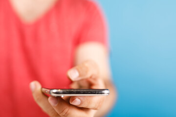A person in a red shirt holds a smartphone, their hand in focus, against a bright blue backdrop. Perfect for concepts like mobile communication,