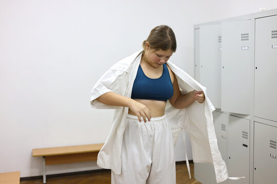 A girl puts on a kimono and ties a belt in the gym locker room.