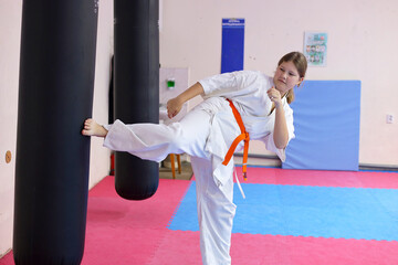 Sportive young girl wearing kimono doing exercises in large sports hall