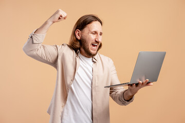 Man celebrating online success, shouting and making a fist pump with laptop