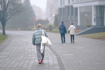 Trendy woman in warm clothes walking alone through dense fog, cold morning, soft mist. Female...
