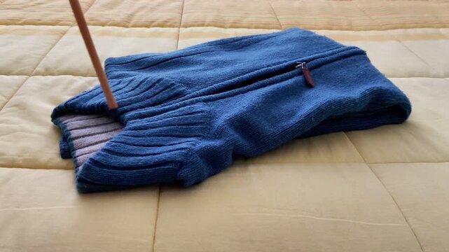 Neatly folded blue sweater with zipper resting on a beige quilted surface, showcasing clean texture, soft fabric detail, and organized presentation in a cozy lifestyle setup