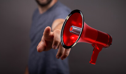 A man's hand pointing at a red megaphone, emphasizing an announcement or a call to action. Ideal for communication, marketing, or advertising co