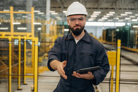 Front view, standing and holding tablet. Warehouse worker in an industrial environment of a factory or storage area - Powered by Adobe