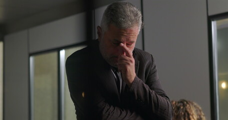 Stressed businessman covering face with hand while standing alone in office conference room during...