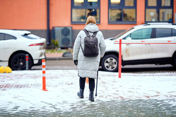 Woman walking carefully across snowy walkway on cold winter day with cane for support. Pedestrian...