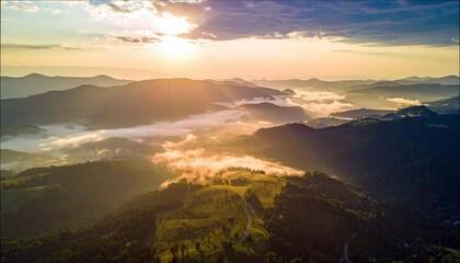 Aerial view of mountains with fog, illuminated by the rising sun, creating a beautiful landscape.