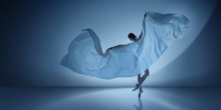 Ballet dancer lifting large white fabric arc on cool blue spotlight. Concept of modern campaign visuals, clean stage design, expressive dance photography.
