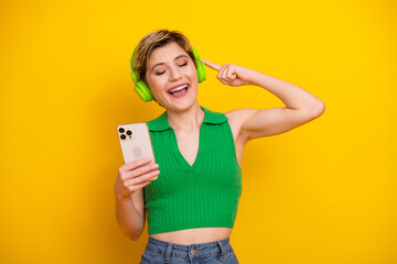 Naklejka premium Happy young woman wearing a green crop top listens to music with bright green headphones on a yellow background for lifestyle fashion and advertising stock photo