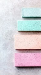 An abstract composition featuring four rectangular blocks in pastel colors arranged on a textured gray surface. The blocks are in shades of blue, green, pink, a