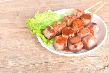 pork sausage roll up bacon stabbing plant stick dressing spicy barbecue sauce arranging with vegetable on plate