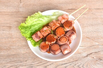 pork sausage roll up bacon stabbing plant stick dressing spicy barbecue sauce arranging with vegetable on plate