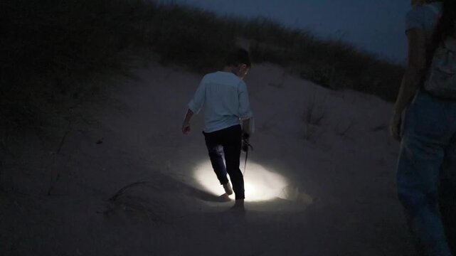 Mother and son exploring sandy dunes at night with flashlight