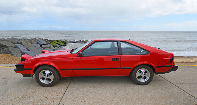 Felixstowe, Suffolk, England - May 04, 2025: Classic Red Toyota Celica Supra parked on seafront promenade beach and sea in background