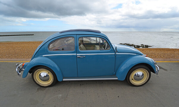 Classic  Blue Volkswagen Beetle  motor car parked on seafront promenade beach and sea in background.