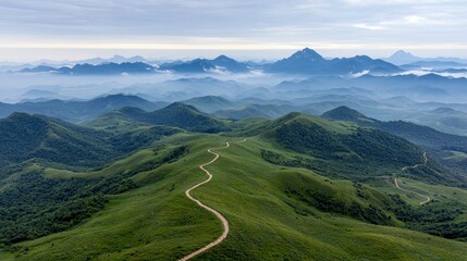 A scenic landscape featuring rolling green hills, a winding road, and distant misty mountain peaks under a cloudy sky.