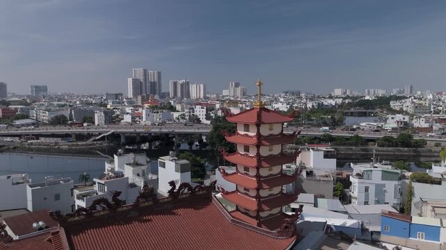 Orbit CCW drone view across Buddhist pagoda in busy urban area of Ho Chi Minh City, Vietnam on a sunny clear day featuring transportation infrastructure of main roads and canals in background