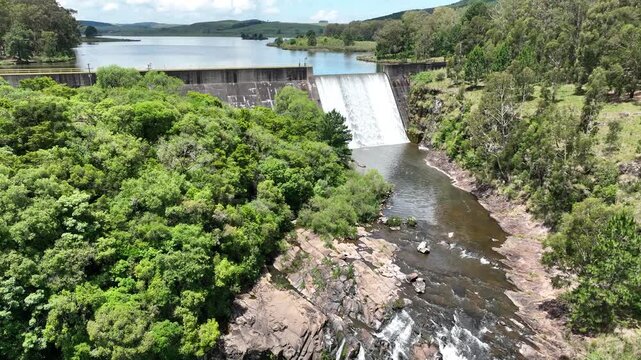 Continuation of previous shot. Drone flies close to the waterfall formed by Barragem do Divisa, then ascends to show the dam and surrounding forested landscape in S&atilde;o Francisco de Paula, RS.