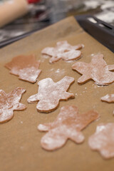 Gingerbread cookies shaped like figures lie on a baking sheet lined with parchment paper, dusted with flour. Perfect for holiday baking, capturing the cozy essence of Christmas cookie preparation