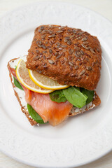 A gourmet smoked salmon sandwich on whole grain bread with flax seeds. Layered with creamy spread, fresh spinach, lemon slices and delicate slices of salmon. A healthy and elegant snack