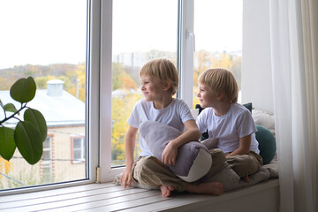 children, blonde twin boys, look out the window, sitting on the window sill