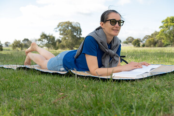 Woman relaxing outdoors with book at park on sunny day.