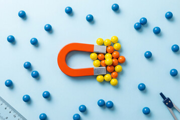 Colorful horseshoe magnet attracting yellow and orange balls on blue background, customer attraction concept.