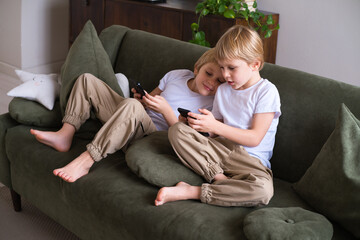 kids blonde boys twins using smartphones on the couch in living room