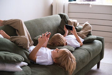 kids boys twins using smartphones lying on the couch