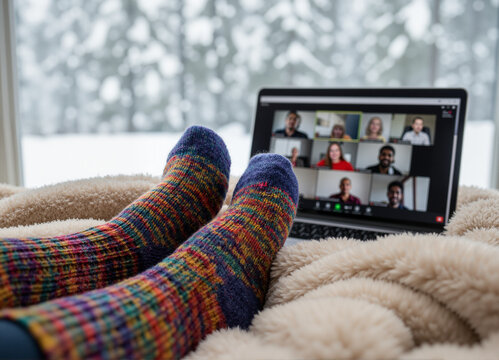 Cozy feet wearing colorful socks resting on a soft blanket while participating in a virtual meeting on a laptop, surrounded by a snowy winter landscape outside the window