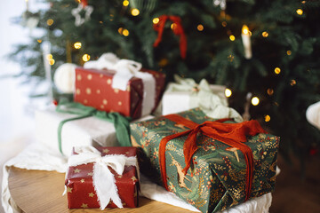 Stylish Christmas gift boxes on table at decorated xmas tree with lights. Merry Christmas and Happy Holidays! Atmospheric winter time. Wrapped Christmas presents banner