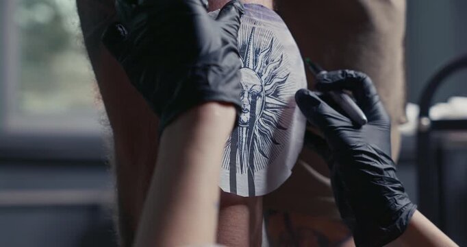 Fresh tattoo stencil of a sun with a face applied to a man's leg, ready for the tattooing process.