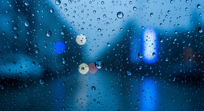 Raindrops on the window. Blue tone raindrops on window with blurred cityscape skyline in background, moody blue tone urban scene ideal for web design, blog header, or print media