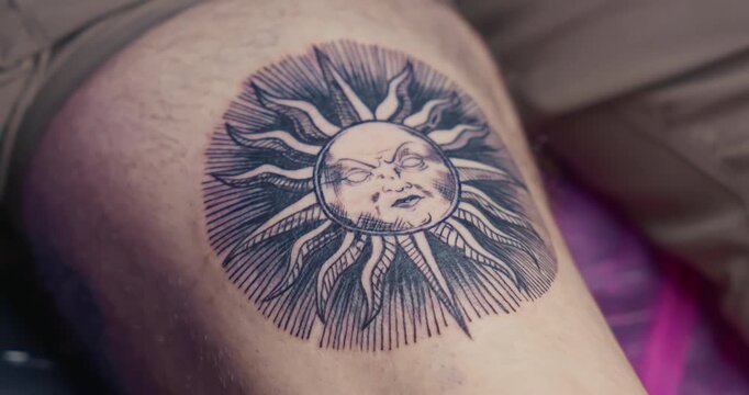  Close-up of a fresh, finished blackwork tattoo of a sun with a face in engraving style on a man's leg