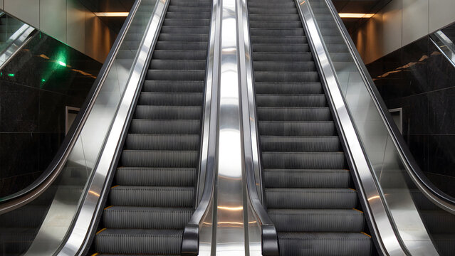 Sleek modern escalator ascends between polished dark marble walls in a contemporary transit hub - Powered by Adobe