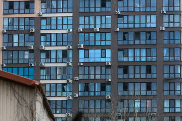 Fototapeta premium A fragment of the facade of a modern multi-story residential building. The building is finished in beige and brown tones. It is part of a new urban development. The windows are broken.