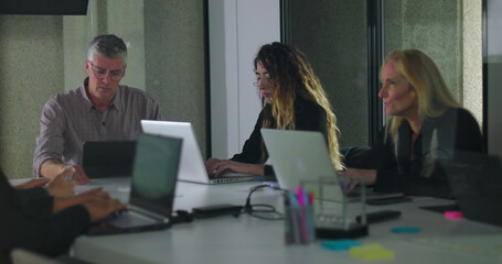 Team working independently on laptops in modern office meeting room with digital display and collaborative environment