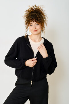 Young woman with curly hair wearing a stylish black hoodie in a bright indoor setting