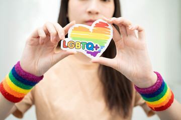Asian woman holding LGBT heart with rainbow flag.