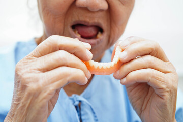 Asian senior woman patient holding teeth denture in her hand for chew food.