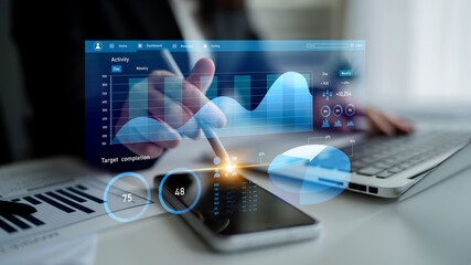 A business professional uses digital tools to analyze performance metrics and create reports with graphs on a smartphone and laptop in a modern office setting. Impute